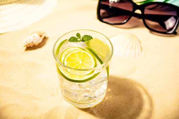 Summer fresh cocktail lemonade water with mint and lime citrus fruit on beach with white sand Summer sea ocean vacation and travel concept