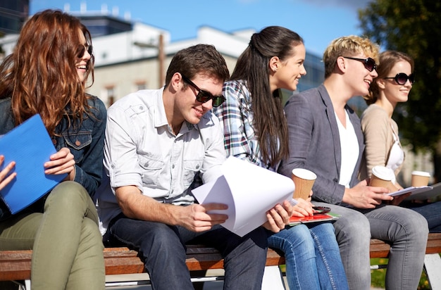 summer, friendship, education and teenage concept - group of happy students with notebooks learning and drinking coffee at campus