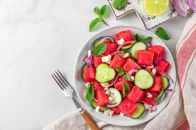 Summer fruit and vegetable salad made of watermelon cucumber soft cheese and onion on white table Top view