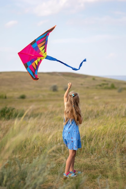 In summer a girl is flying a kite on the field Plays outdoors in the park at sunset The child plays in nature