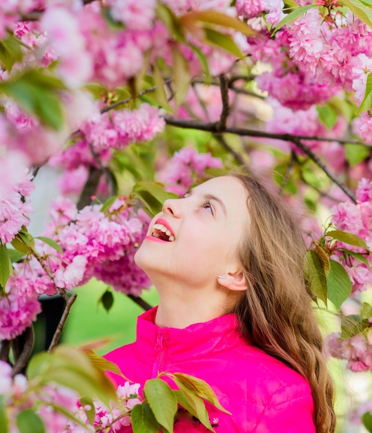 Summer holiday Childhood beauty happy girl in cherry flower Sakura tree blooming small girl in spring flower skincare spa Natural cosmetics for skin blossom smell allergy Express positivity