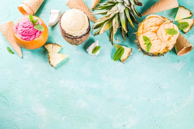 Summer holiday vacation concept, set various tropical ice cream sorbets, frozen juices in pineapple, grapefruit and coconut, light blue concrete 