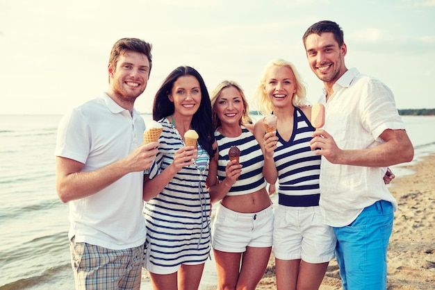 summer, holidays, sea, tourism and people concept - group of smiling friends eating ice cream on beach