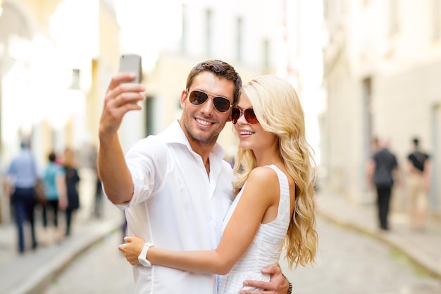 summer holidays, technology, love, relationship and dating concept - smiling couple taking picture with smartphone in the city