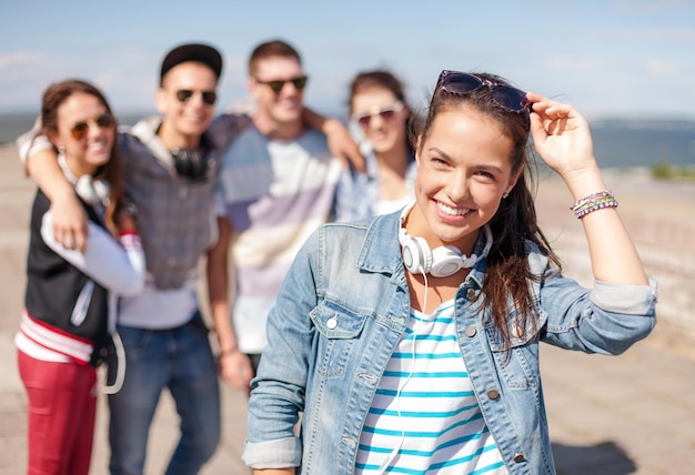 summer holidays and teenage concept - teenage girl in sunglasses and headphones hanging out with friends outside