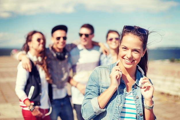 summer holidays and teenage concept - teenage girl in sunglasses and headphones hanging out with friends outside