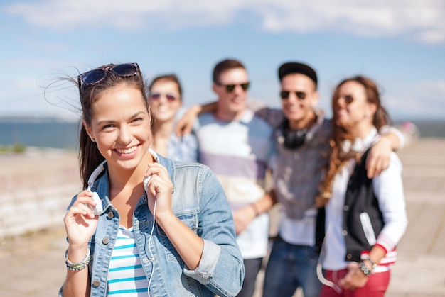 summer holidays and teenage concept - teenage girl in sunglasses and headphones hanging out with friends outside