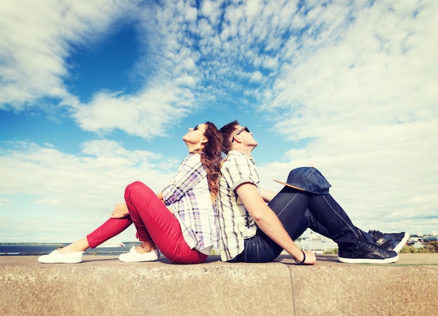 summer holidays and teenage concept - teenagers sitting back to back and looking up in the sky