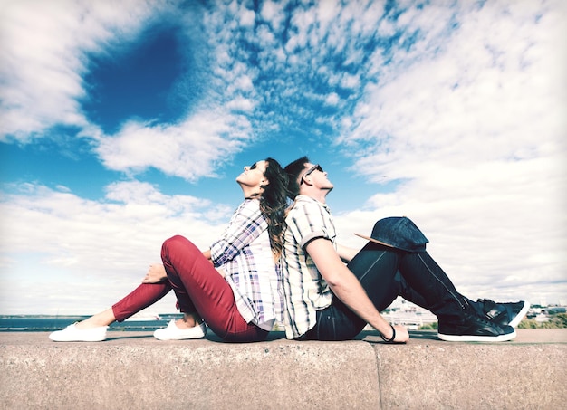 summer holidays and teenage concept - teenagers sitting back to back and looking up in the sky