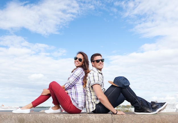 summer holidays and teenage concept - teenagers sitting back to back