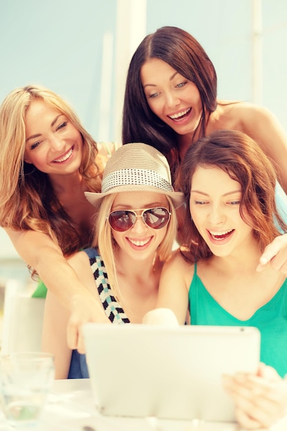 summer holidays, vacation, internet and technology concept - smiling girls looking at tablet pc in cafe