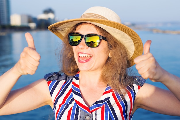 Summer holidays and vacation - young woman showing thumbs up on the beach.