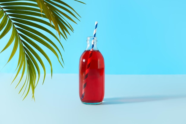 Summer iced cranberrie punch cocktail in bottle with palm leaf on blue background