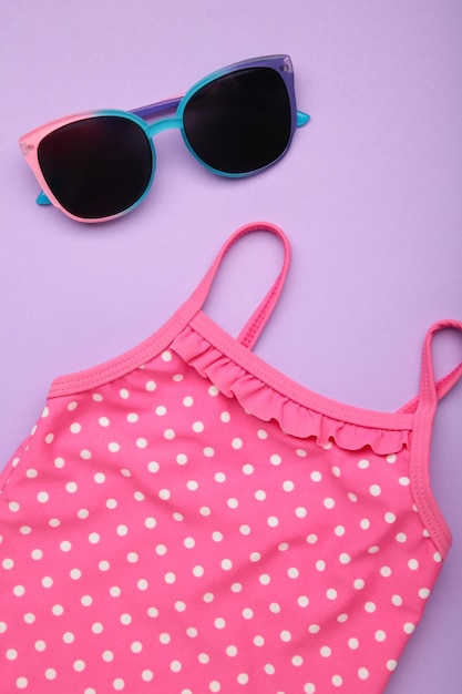 Summer kid's vacation concept swimsuit with cute sunglasses on purple background Holiday concept fashion child