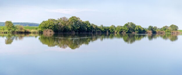 Summer landscape panorama with river and trees reflected in river water