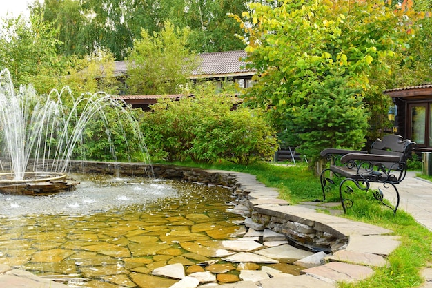 Summer landscape with a beautiful carved beautiful bench at the fountain. A cozy quiet place to relax in nature.