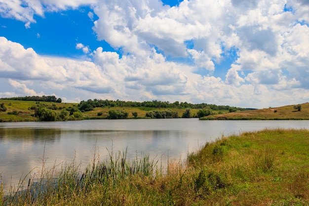 Summer landscape with beautiful lake, green meadows, hills, trees and blue sky