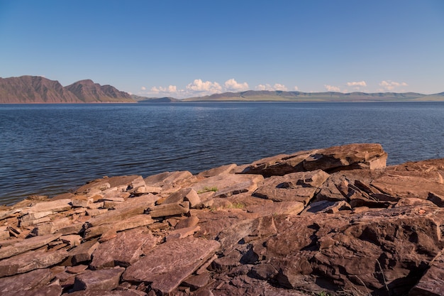 Summer landscape with a reservoir a rocky shore in the foreground and mountains