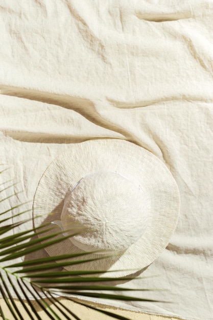 Summer lifestyle background top view sun hat under green palm leaves on beach towel on sand