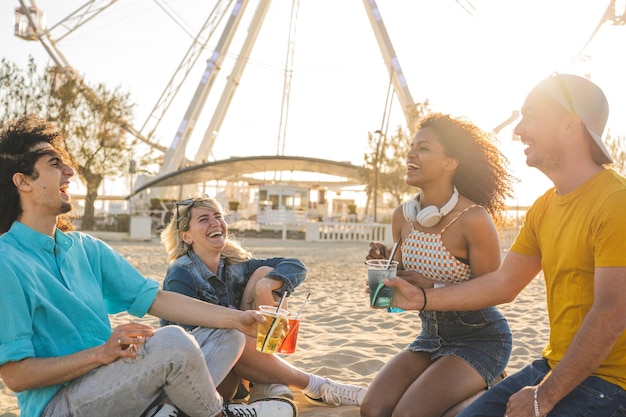 Summer lifestyle concept with friends having fun together and drinking coktail sitting on beach happy guys and girls students cheering at sunset on vacation days celebration moments on holiday