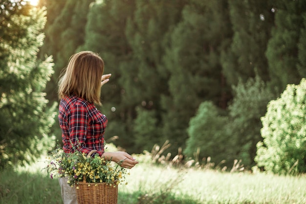 Summer lifestyle portrait of a beautiful young woman smiling and holding a basket with a bouquet of wild flowers The concept of happiness and love