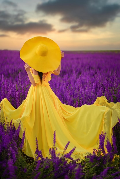 Summer mood. A woman in a luxurious yellow dress is standing in a purple flowering field with her back to the camera.