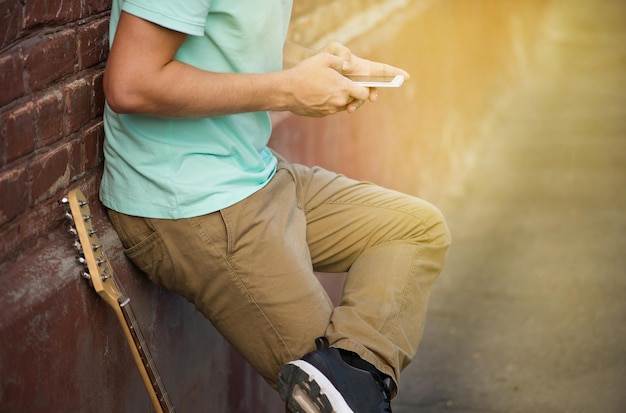 Summer party young stylish guy standing near brown brick wall hands holding mobile phone