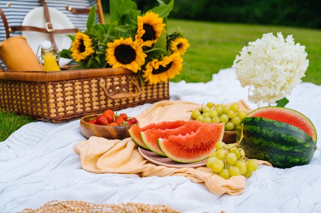 Summer picnic concept on sunny day with watermelon, fruit, bouquet hydrangea and sunflowers flowers.