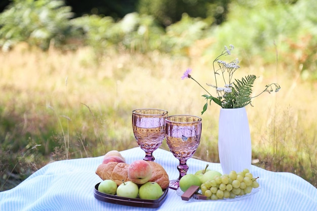 Summer picnic with croissants fruits chocolate and glasses of wine in the forest Cottage core aesthetic Summer vibe Copy space