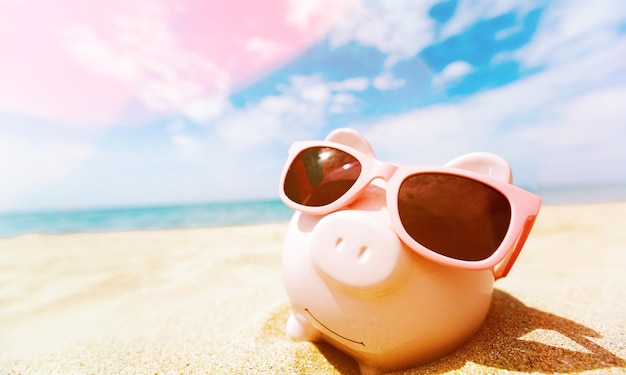 Summer piggy bank with sunglasses on the beach