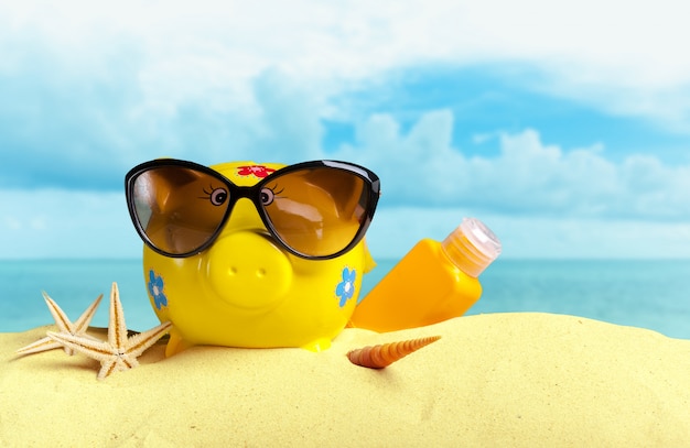 Summer piggy bank with sunglasses on the beach