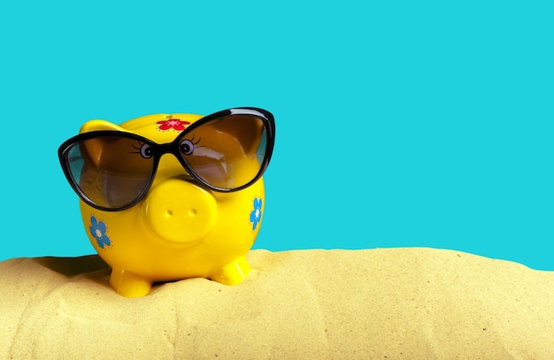 Summer piggy bank with sunglasses on the beach