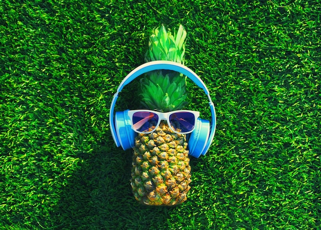 Photo summer pineapple with wireless headphones listening to music on the grass background top view