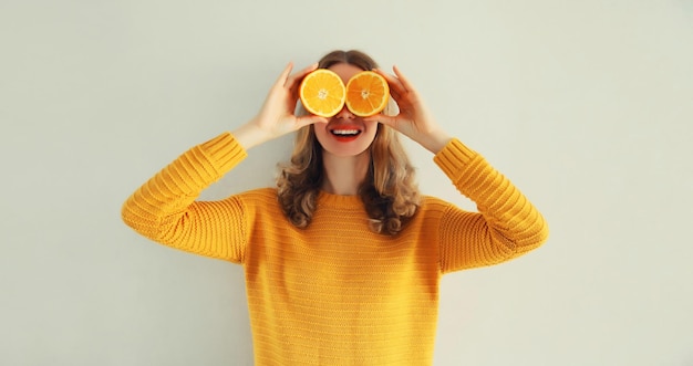 Photo summer portrait of happy cheerful woman covering eyes with slices of orange looking for something