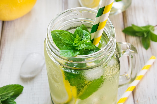 Summer refreshing detox cocktail. Water with lemon, mint and ice in mason jar on wooden board. 