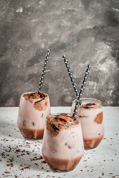 Summer refreshment drinks. Chilled iced chocolate cocoa. With scoop of chocolate ice cream, chocolate powder and ice. In glasses, with tubes for drinking. White concrete table. 