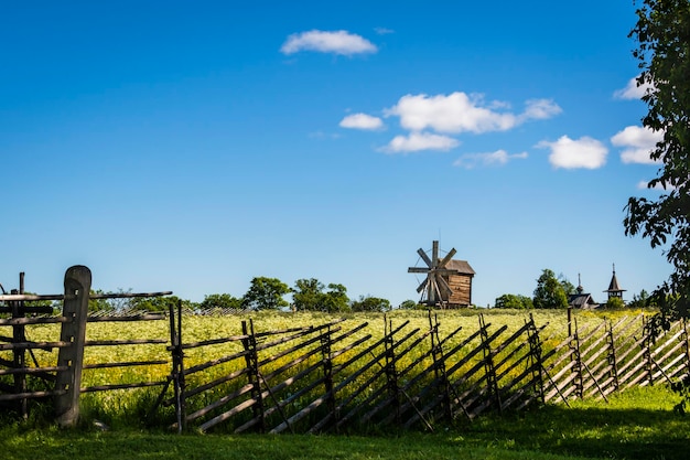 Summer rural landscape behind a wooden fence an old windmill and a wooden church