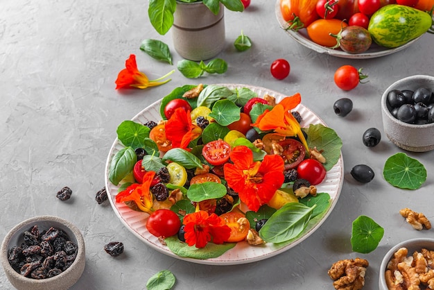 Summer salad with nasturtium flowers tomatoes olives raisins and nuts on gray background Healthy diet food