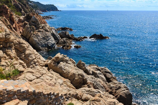 Summer sea rocky coast view with sunny sparkles on water surface and stony stairs (Costa Brava, Spain).