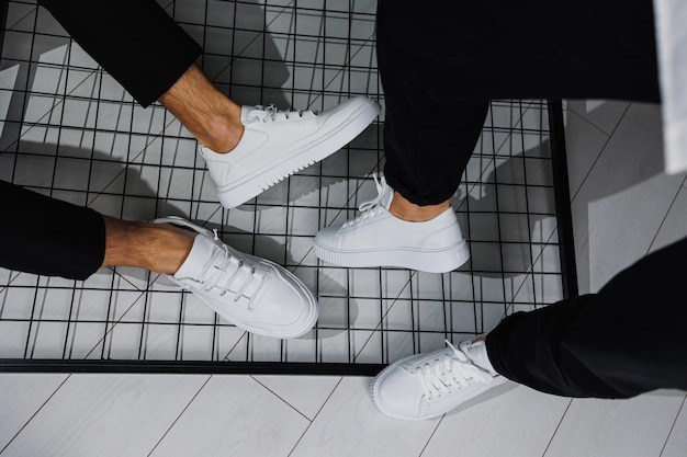 Summer shoes Closeup of male and female legs in black pants and white casual sneakers Summer leather shoes for men and women