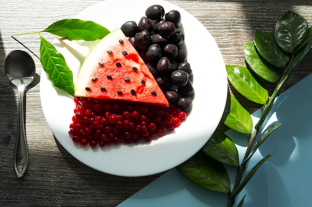 Summer snack Fresh berries and fruits on a wooden table with green leaves of plants