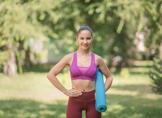 Summer sportswoman in the park with a carpet in her hands