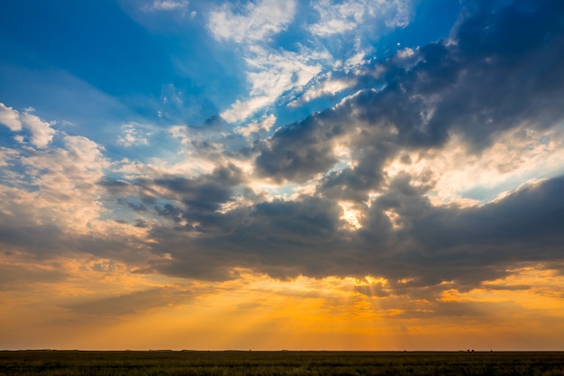 Summer steppe plain. Colorful sunset with many illuminated clouds