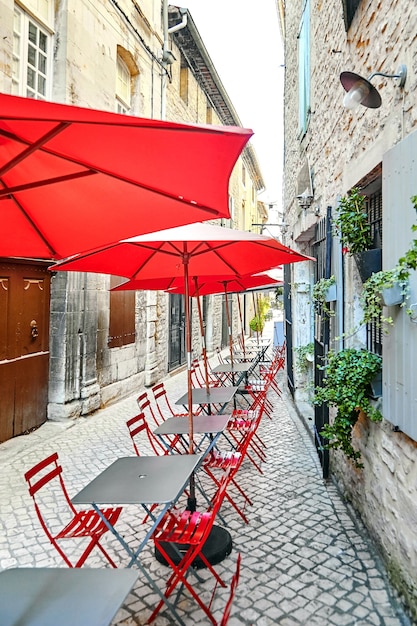 Summer street cafe with red umbrellas and chairs. Empty gray tables. Outdoor a french tourist restaurant in beautiful old town. France, Europe