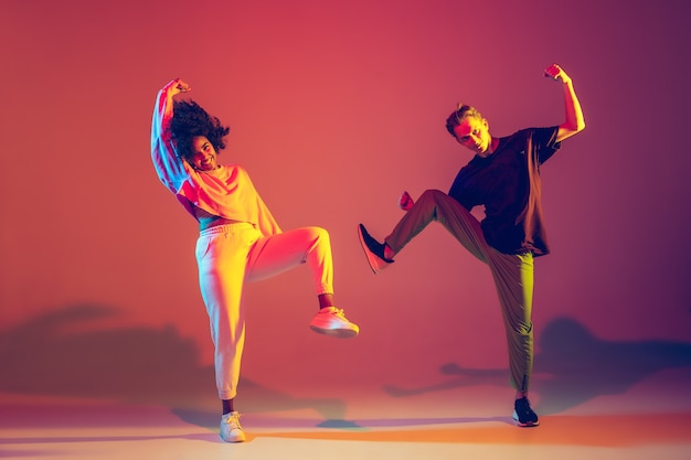 Summer. Stylish man and woman dancing hip-hop in bright clothes on green background at dance hall in neon light. Youth culture, movement, style and fashion, action. Fashionable portrait.