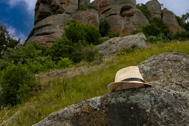 Summer sun hat made of straw lies on a large stone against the backdrop of rocky mountains