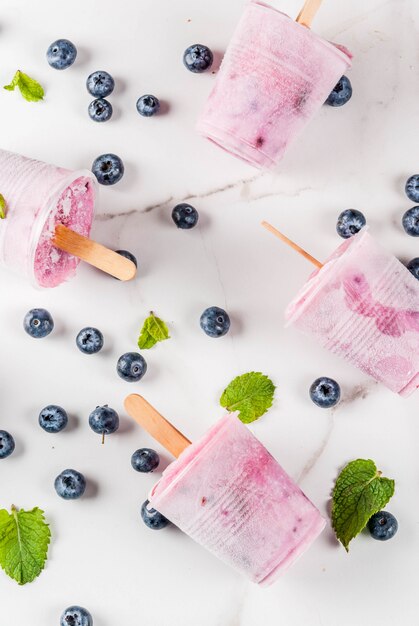 Summer sweets and desserts. Vegan food. Frozen drinks, smoothies. Ice cream popsicles from homemade Greek yogurt and fresh organic blueberries. With mint. On white marble table. copyspace top view