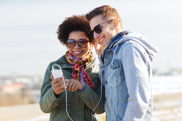 summer, technology, people and friendship concept - smiling couple with smartphone and earphones listening to music on city street