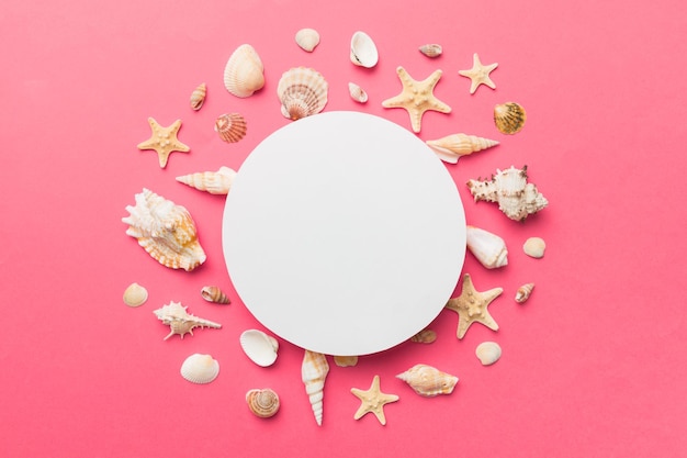 Summer time concept with blank greeting card and blank white paper on colored background Seashells from ocean shore in the shape of frame separated with space for text top view