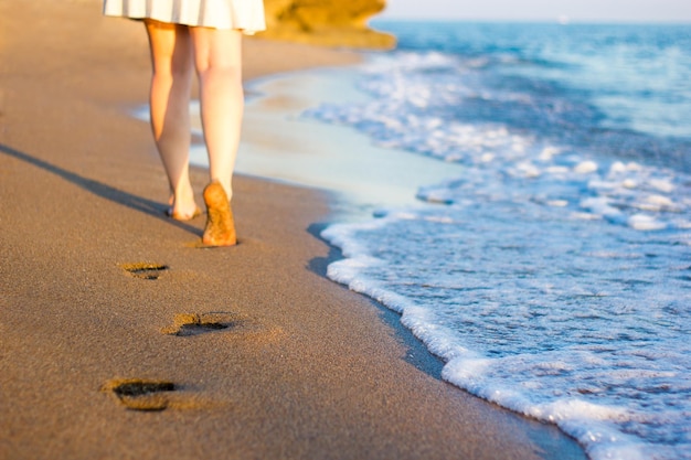 Photo summer and travel close up of female legs and footprints on the sunset beach